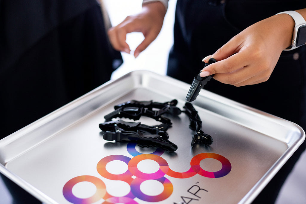 Person handling black plastic clips on a tray with a colorful logo in the background