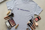 Gray t-shirt with 'QC Makeup Academy' logo surrounded by makeup items on a light surface.