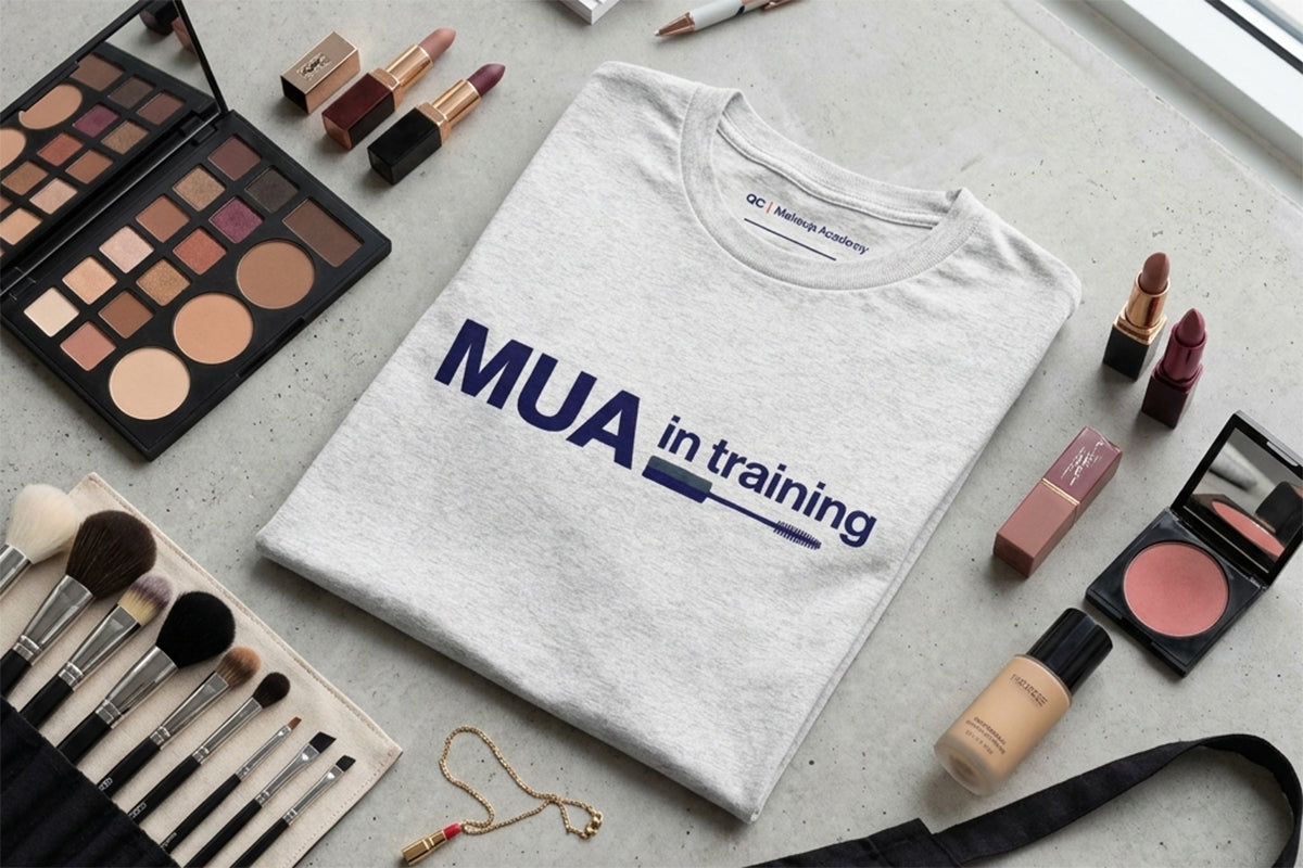 White t-shirt with 'MUA in training' text surrounded by makeup tools on a light surface.