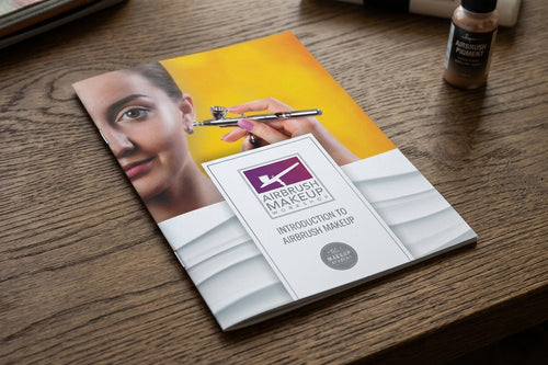 Makeup tutorial book on a wooden surface with a bottle of airbrush makeup.