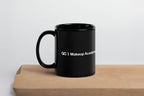 Black mug with 'QC Makeup Academy' text on a wooden surface and light gray background