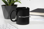 Black mug with 'QC Event School' logo on a desk with a plant and books in the background