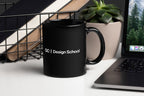 Black mug with 'QC Design School' on a desk with a laptop and plant