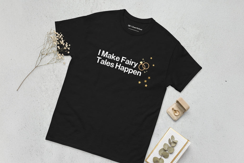 Black t-shirt with 'I Make Fairy Tales Happen' text on a light gray surface.
