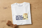 White t-shirt with a graphic of a dog and text 'Tell Your Dog I Said Nice Haircut' on a wooden surface.