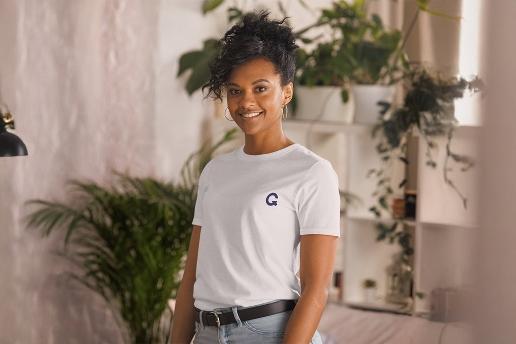 Person wearing a white t-shirt with a QC logo in a room with plants