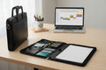 Black portfolio organizer, laptop, and office supplies on a desk.