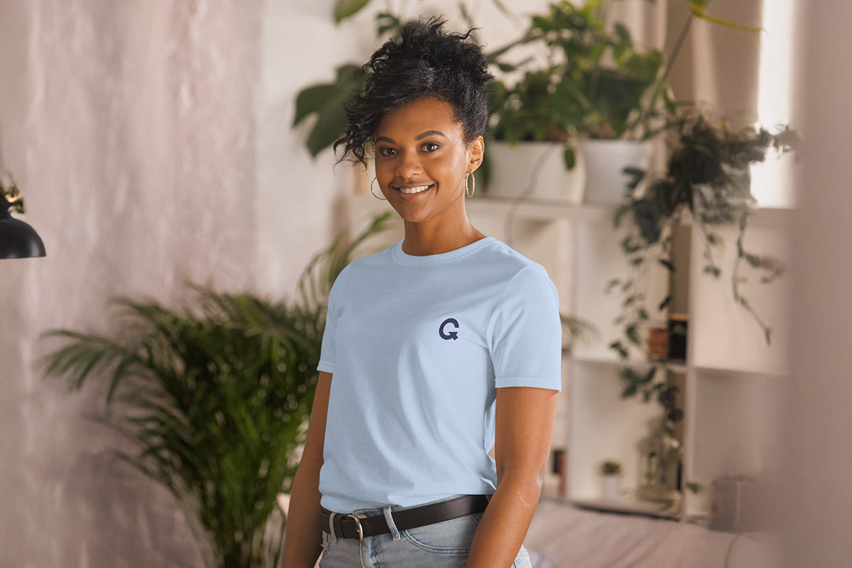 Person wearing a light blue t-shirt with a QC logo in a room with plants