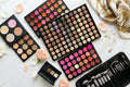 Makeup palettes with various colors and makeup brushes on a light surface.