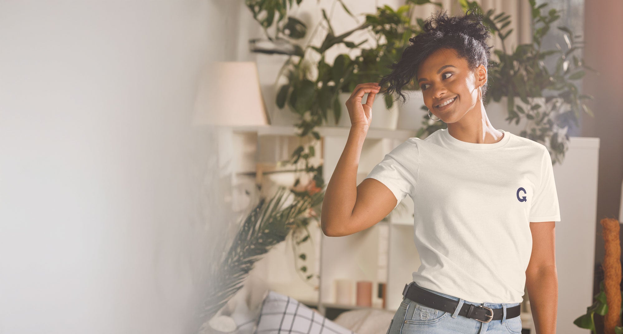 Woman wearing a white t-shirt with a Q logo in a room with plants and decor