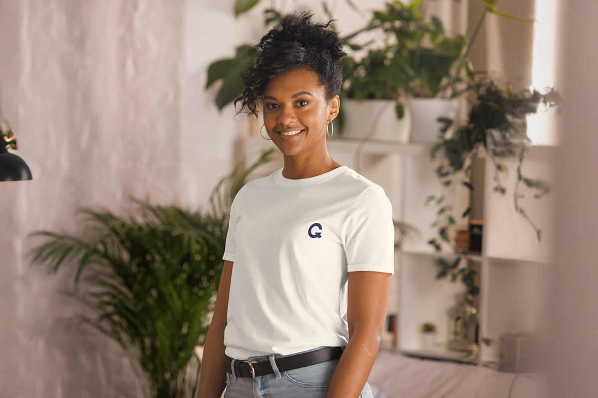 Person wearing a white t-shirt with a QC logo in a room with plants