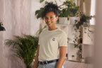 Person wearing a light-colored t-shirt with a QC logo in an indoor setting with plants.