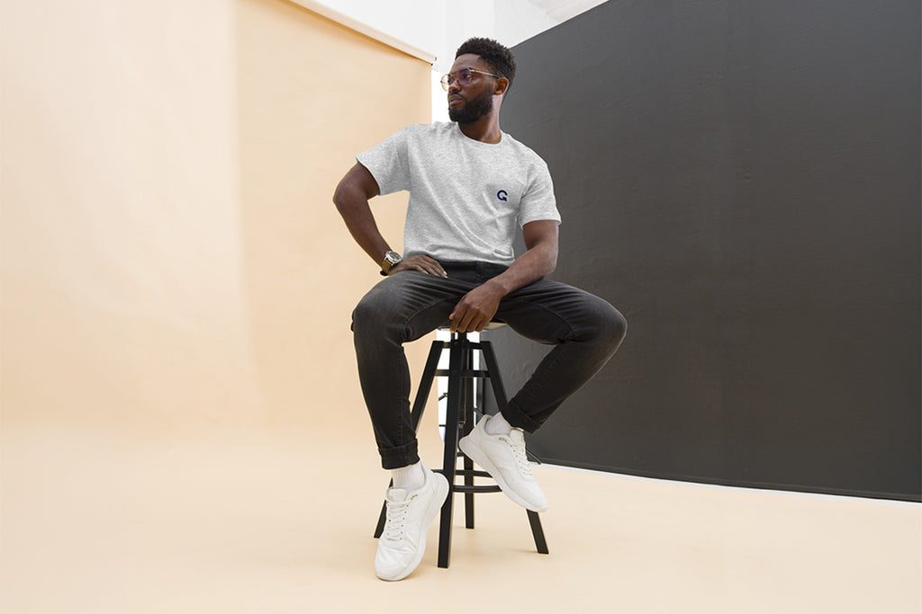 Man sitting on a stool wearing QC Design School shirt against a plain background
