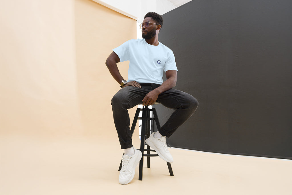 Man sitting on a stool wearing light blue QC Design School shirt against a plain background