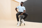 Man sitting on a stool wearing light blue QC Design School shirt against a plain background