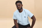 Man wearing a light blue t-shirt with a 
Q logo on a beige background