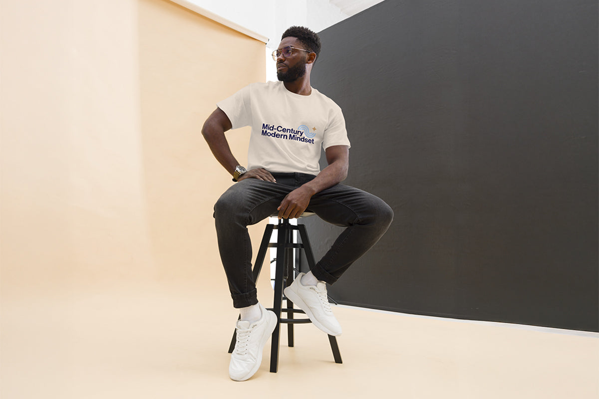 Man sitting on a stool wearing a t-shirt that reads "Mid-Century Modern Mindset" against a plain background