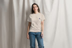 Woman wearing a beige t-shirt with a Q logo and blue jeans against a plain background