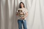 Woman holding a small dog in front of a plain background