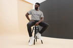 Man sitting on a stool wearing a gray t-shirt with "QC Design School" and dark pants.