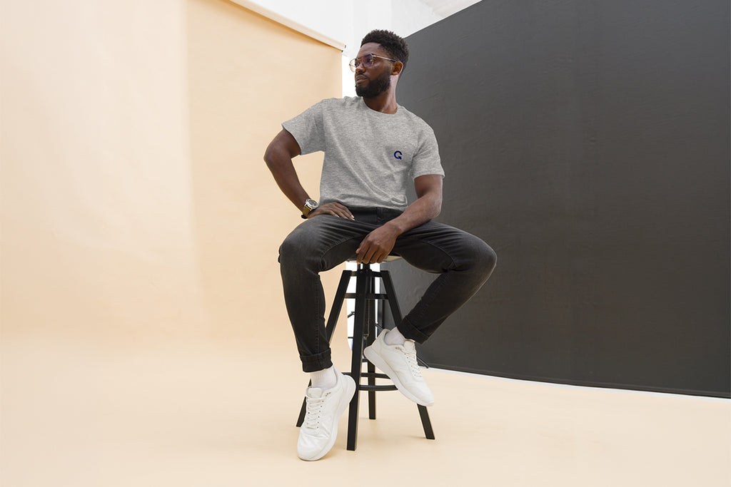 Man sitting on a stool wearing gray QC Design School shirt against a plain background