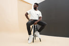 Man sitting on a stool wearing a QC Design School shirt against a plain background