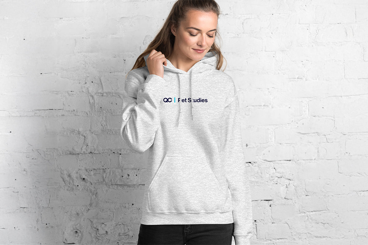 Person wearing a gray hoodie with QC Pet Studies text on a white brick wall