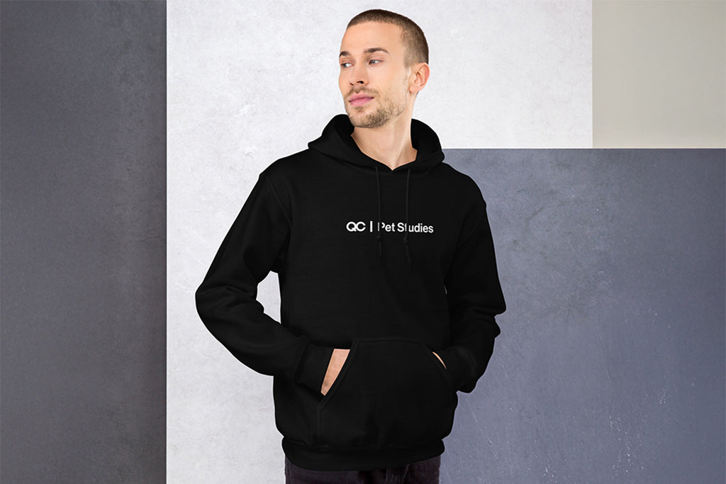 Man wearing a black hoodie with QC Pet Studies text on it against a gray wall.
