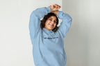 Person wearing a light blue hoodie with a QC Makeup Academy logo on a plain background