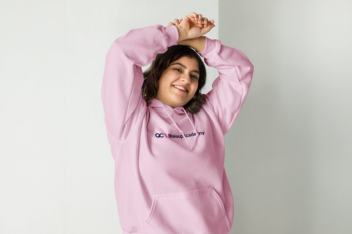 Person wearing a pink hoodie with a QC Makeup Academy logo on a plain background