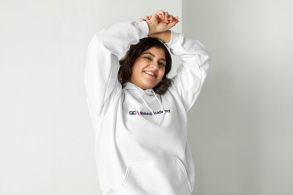 Person wearing a white hoodie with a QC Makeup Academy logo on a plain background