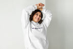 Person wearing a white hoodie with a QC Makeup Academy logo on a plain background