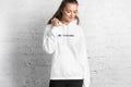 Person wearing a white hoodie with a QC Pet Studies logo against a white brick wall