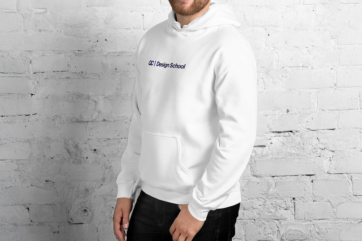 Person wearing a white hoodie with QC Design School text against a white brick wall