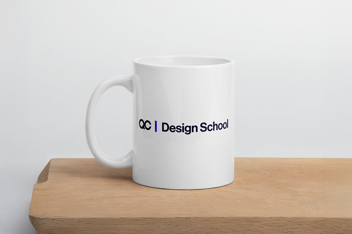 White mug with 'QC Design School' text on a wooden surface and light gray background