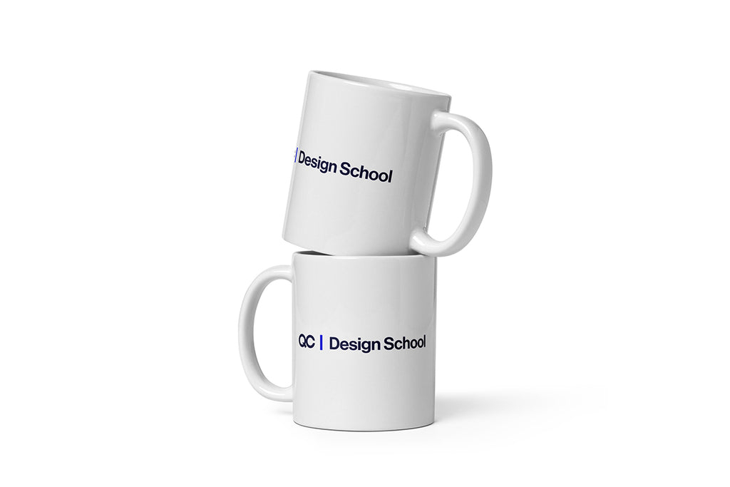 Two white mugs with 'QC Design School' text on a white background