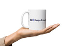 White mug with 'QC Design School' logo held in a hand on a white background