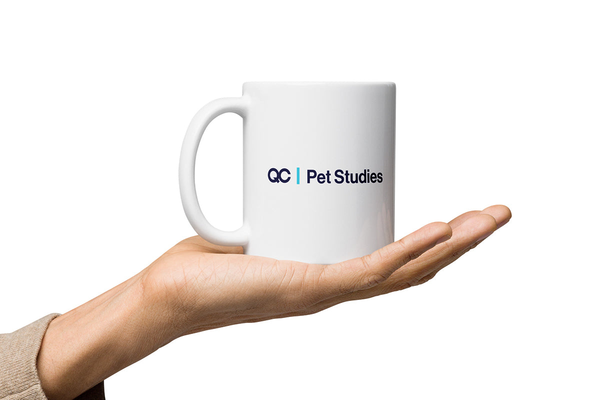 White mug with 'QC Pet Studies' logo held in a hand on a white background