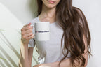Woman holding a white mug with 'QC Makeup Academy' text against a plain background