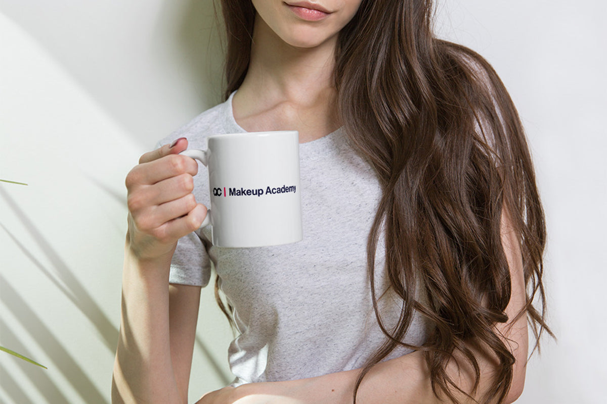Woman holding a white mug with 'QC Makeup Academy' text against a plain background