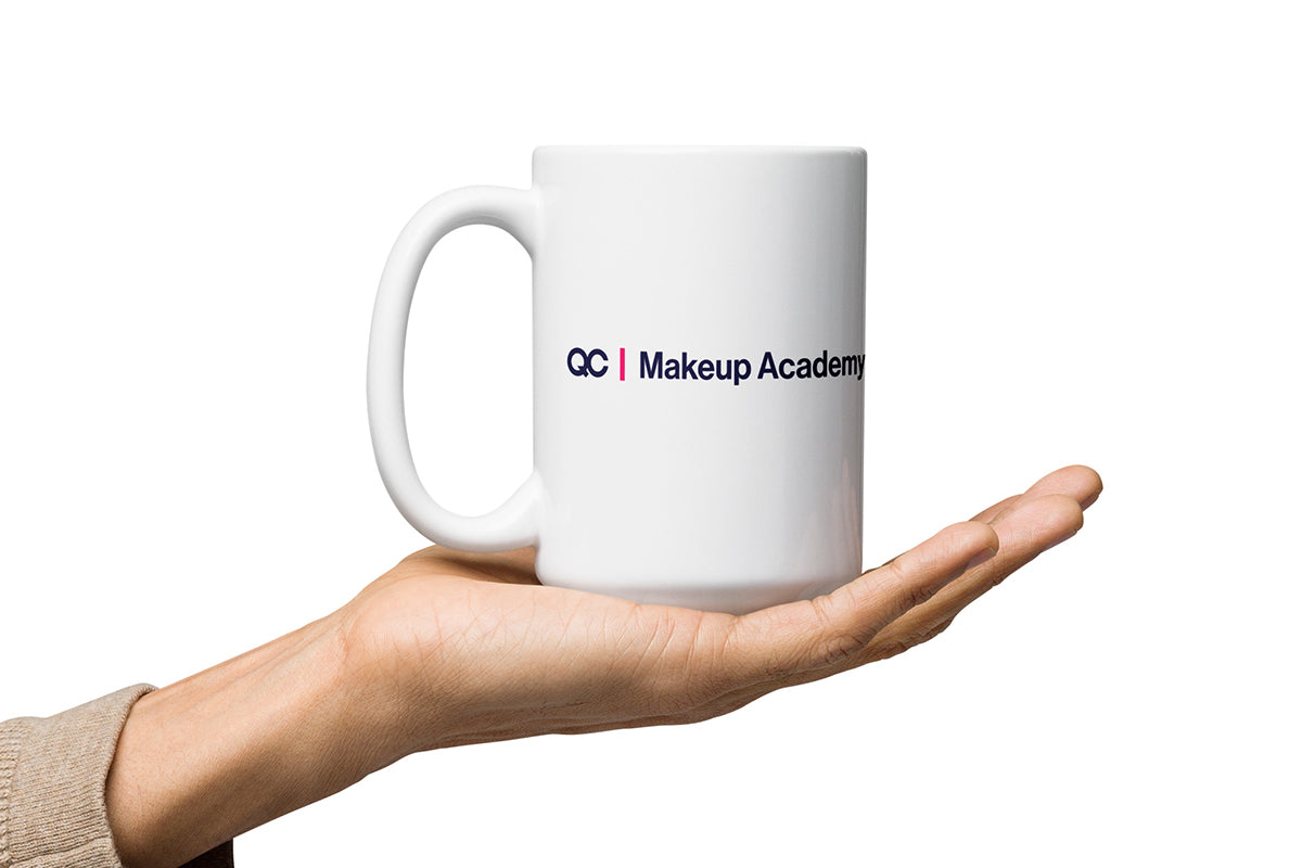 White mug with 'QC Makeup Academy' logo held in a hand on a white background