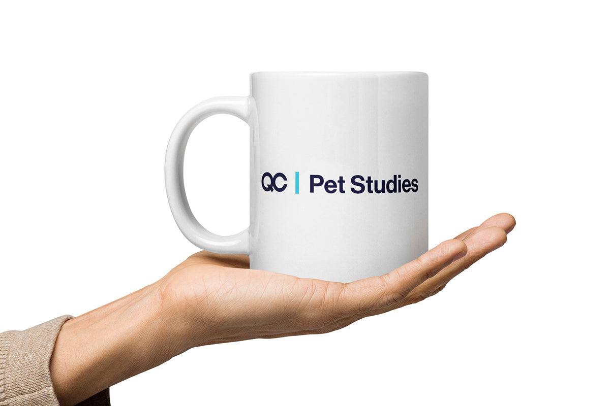 White mug with 'QC Pet Studies' logo held in a hand on a white background