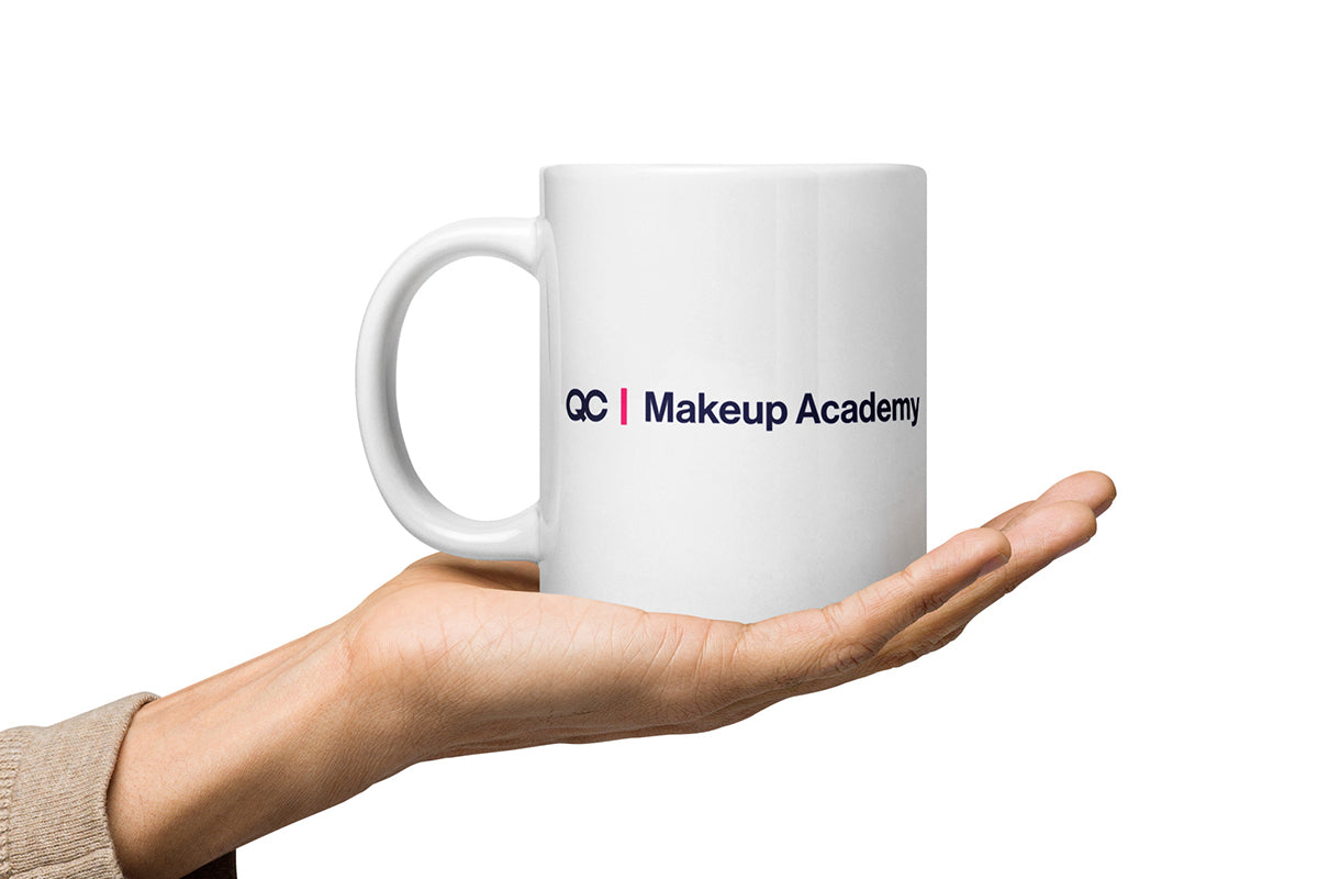 White mug with 'QC Makeup Academy' text held in a hand on a white background