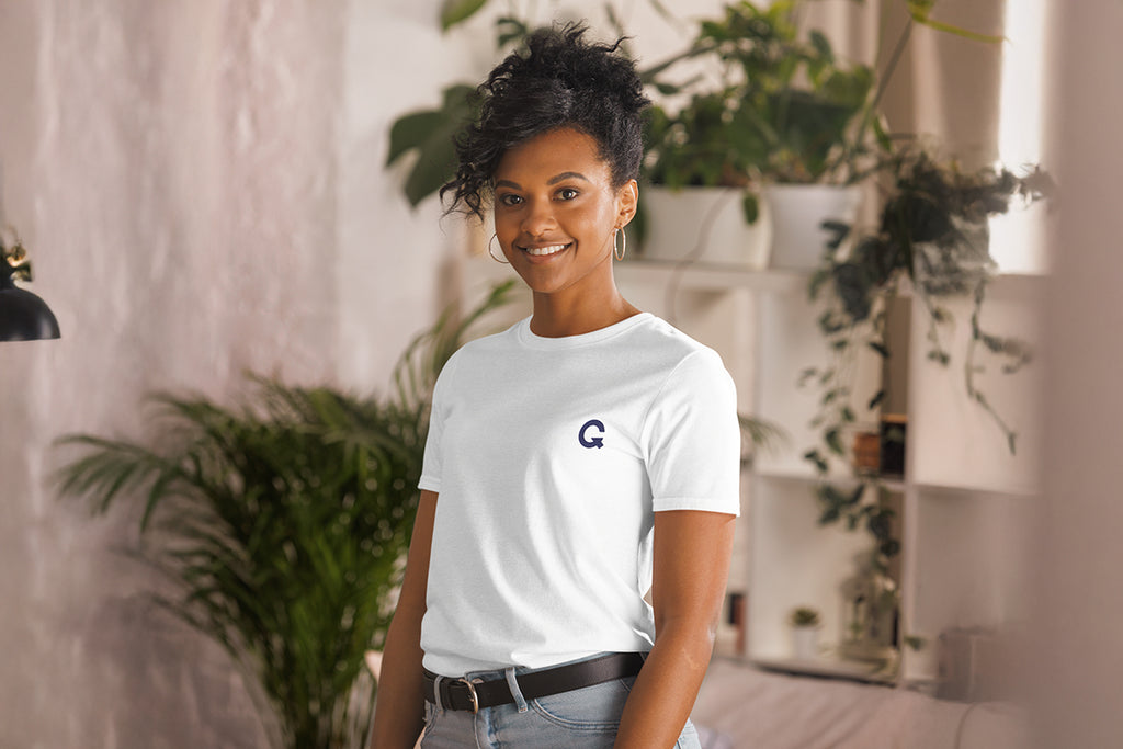 Person wearing a white t-shirt with a QC logo in an indoor setting with plants