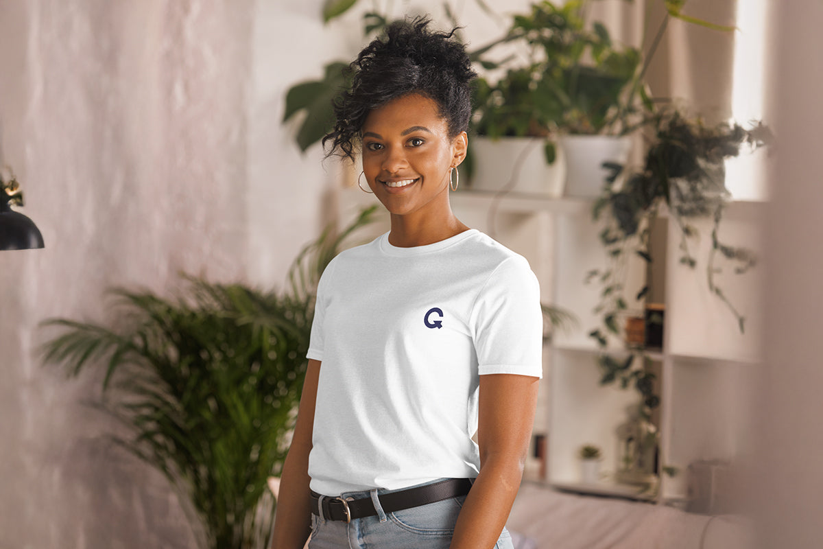 Person wearing a white t-shirt with a QC logo in an indoor setting with plants