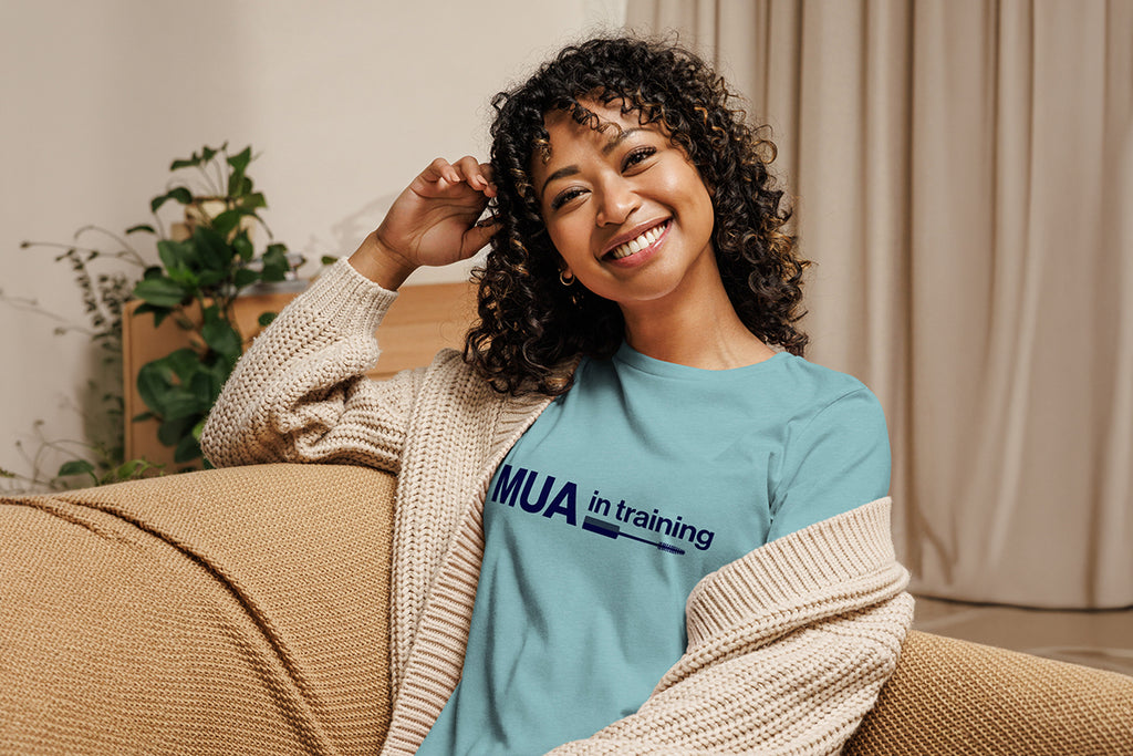 Woman wearing a blue 'MUA in training' shirt sitting on a couch.