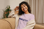 Woman wearing a purple 'MUA in training' shirt sitting on a couch.