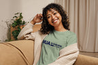 Woman wearing a green 'MUA in Training' shirt sitting on a couch.