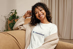 Woman wearing an off-white t-shirt with 'QC Event School' logo, sitting on a couch in a cozy indoor setting.