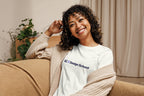 Woman wearing a 'QC Design School' t-shirt sitting on a couch in a cozy room.